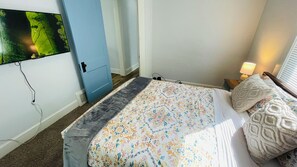 Une chambre à coucher avec un lit, un téléviseur fixé au mur, une table de chevet avec une lampe et une porte.