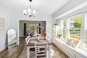A dining area with a wooden table, white chairs, a chandelier, and a view of a garden through large windows. - Brand new Apartment in West Cleveland (Cleveland)