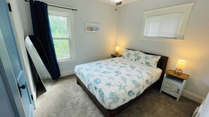 A bedroom with a bed, two bedside lamps, a window with blinds, a door, and a picture on the wall. - Your Coastal Getaway in West Cleveland! (Cleveland)