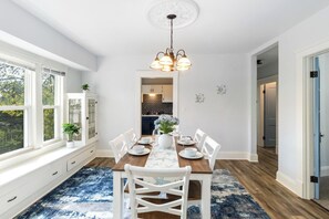 A dining area with a wooden table set for four, white chairs, and a chandelier. - Your Coastal Getaway in West Cleveland! (Cleveland)