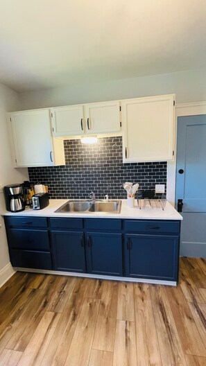 A kitchen with a central island, white cabinets, a black tiled backsplash, and wooden flooring. - Your Coastal Getaway in West Cleveland! (Cleveland)