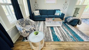 A living room with a blue sofa, patterned armchair, coffee table, and a blue and white striped rug. - Your Coastal Getaway in West Cleveland! (Cleveland)