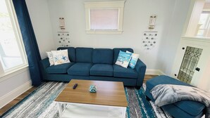 Una sala de estar con un sofá azul, una mesa de centro de madera y una alfombra estampada.