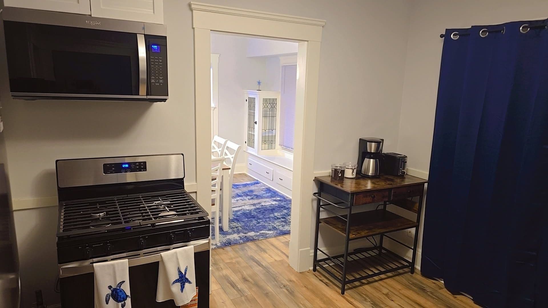 A compact kitchen with a stove, microwave, and a coffee maker on a small table.