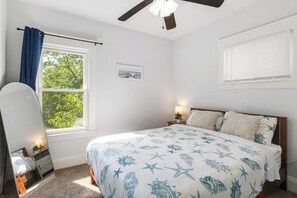 A bedroom with a bed, a ceiling fan, a window with curtains, a bedside lamp, and a small plant. - Your Beachy Getaway in West Cleveland! (Cleveland)