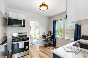 A modern kitchen with stainless steel appliances, a window with blue curtains, and a view of the outside. - Your Beachy Getaway in West Cleveland! (Cleveland)