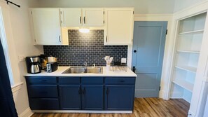 Een kleine keuken met een zwart betegelde achterwand, witte bovenkastjes en een blauw aanrecht.