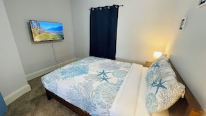Een slaapkamer met een bed, een aan de muur bevestigde televisie en een raam met gordijnen.