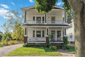 A two-story house with a front porch, a brick foundation, and a large tree in the foreground. - Your Beachy Getaway in West Cleveland! (Cleveland)