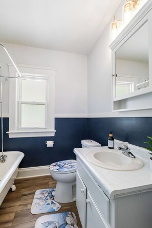 A bathroom with a white sink, a toilet, a mirror, and a window. - Your Beachy Getaway in West Cleveland! (Cleveland)