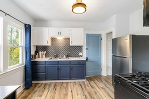 Eine moderne Küche mit weißen Schränken, einer schwarzen Spritzschutzwand, einer blauen Tür und einem Edelstahl-Kühlschrank.