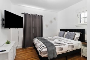 Ein Schlafzimmer mit Bett, Wandfernseher, Fenster und Nachttisch.