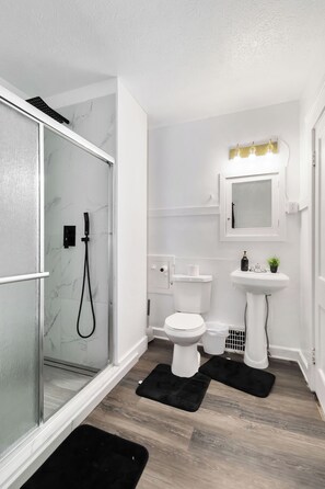 Ein modernes Badezimmer mit Duschkabine aus Glas, Toilette, Standwaschbecken und einem beleuchteten Spiegel.