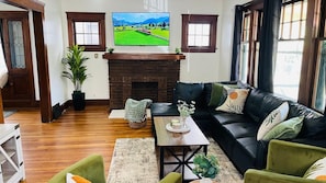 A living room with a fireplace, a black leather sofa, a wooden coffee table, and a television mounted above the fireplace. - Single Family house Close to Freeway for easy access to everywhere in Cleveland! (Cleveland)
