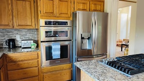 A kitchen with wooden cabinets, stainless steel appliances including a refrigerator, oven, and microwave, and a granite countertop. - Welcome to your perfect Pacific Northwest retreat! 🌲 Located on a peaceful Beaverton cul-de-sac, this 2-story home is close to Nike HQ & Intel. Enjoy fast WiFi, 3 Smart TVs, and a basketball hoop! The perfect blend of tranquility and convenience! ✨ (Beaverton)