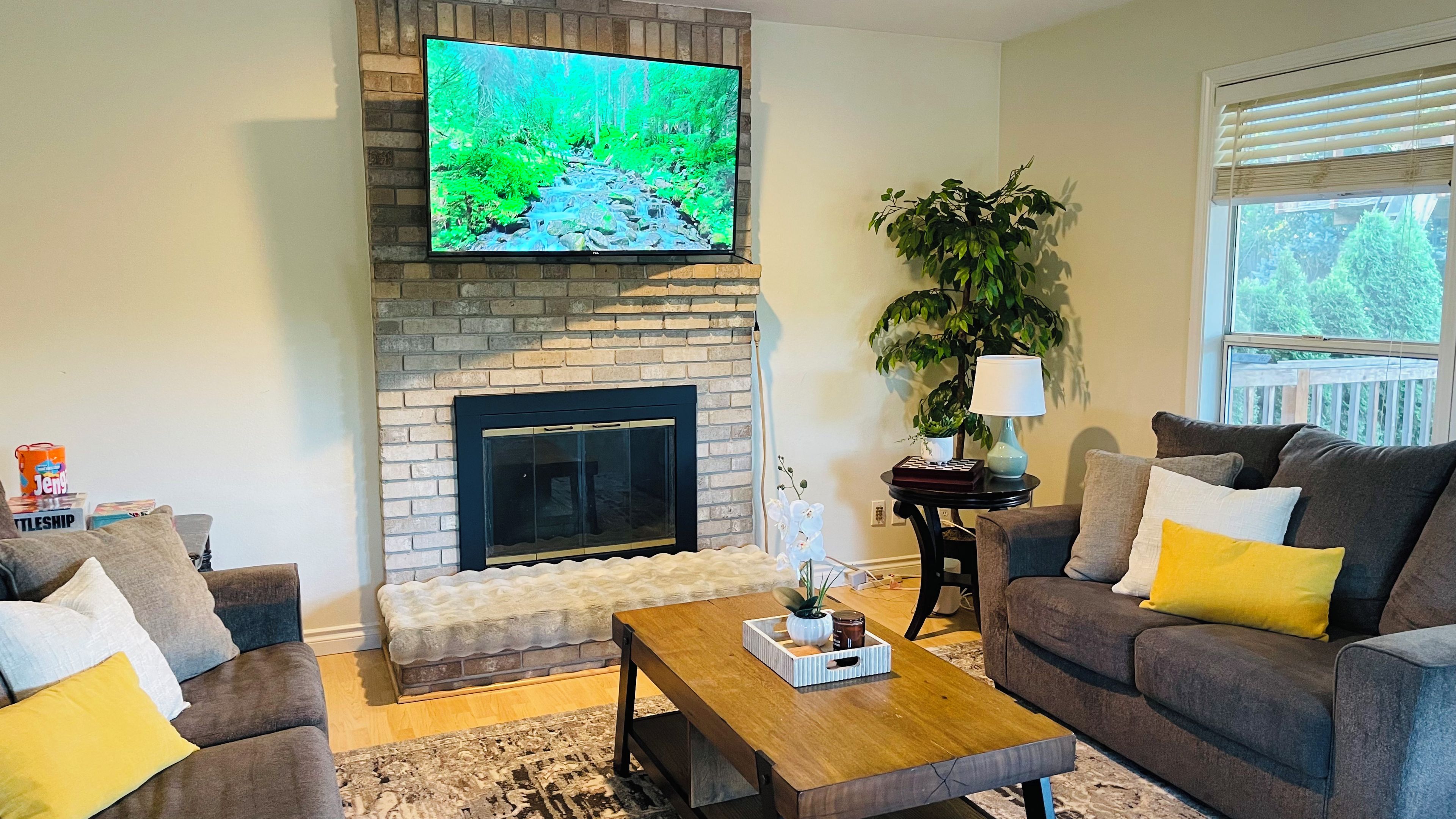 Una sala de estar con chimenea, televisor montado arriba y un sofá con cojines.