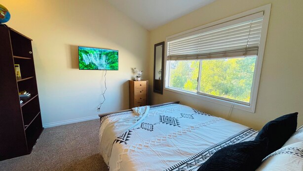 Een slaapkamer met een bed, een dressoir, een televisie en een raam met zonwering.