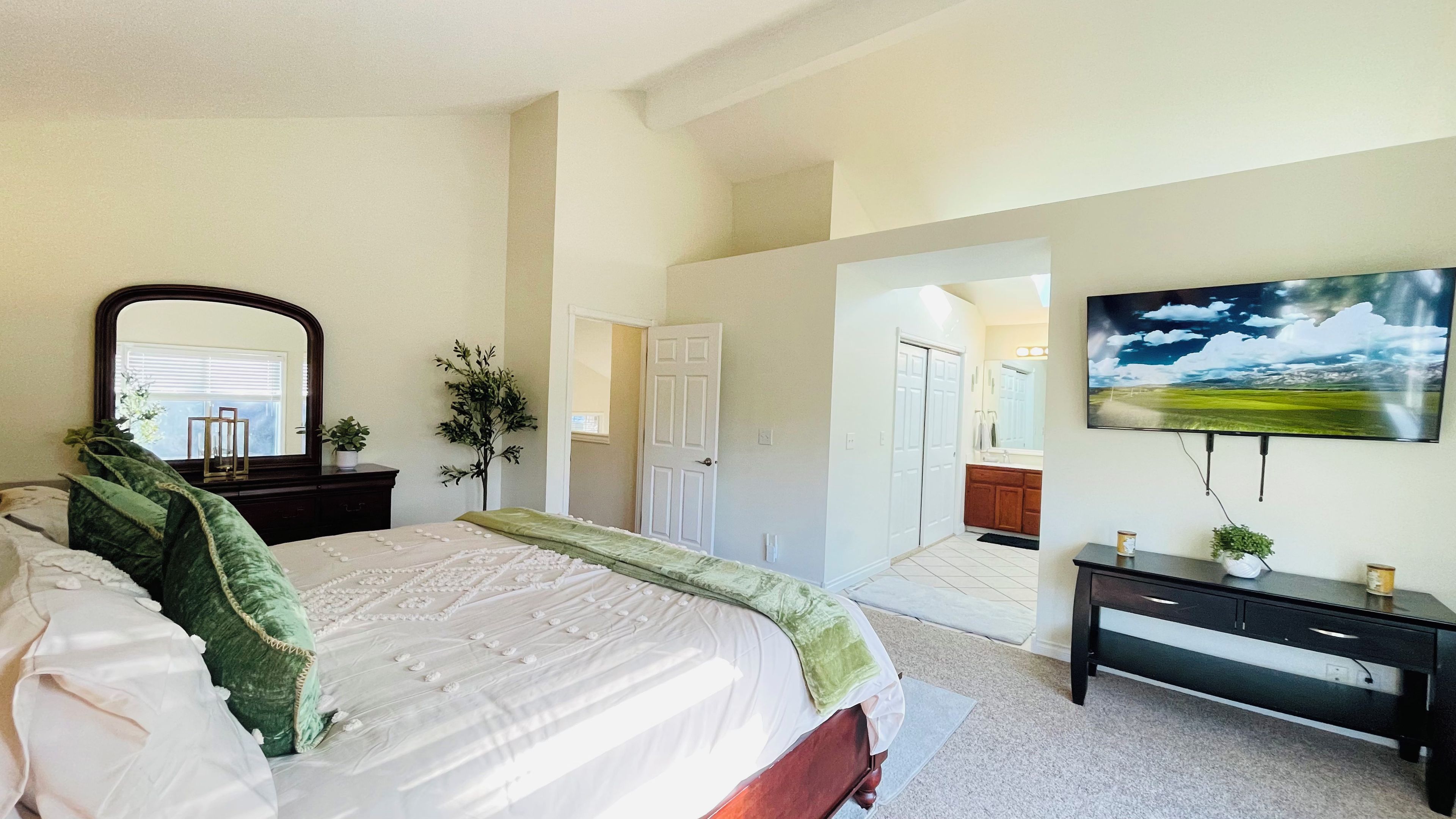 A bedroom with a bed, a dresser, a mirror, a door leading to a bathroom, and a TV mounted on the wall.