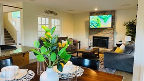 A living room with a fireplace, a flat-screen TV, a dining area with a table set for two, and a staircase leading to another level.