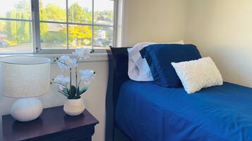 A bedroom with a bed, a nightstand, a lamp, and a window with a view of trees and parked cars.