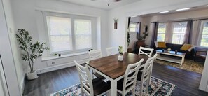 A dining area with a wooden table and white chairs, a sofa, and a window with blinds. - Recent  Remodeled UP Unit 3bedroom in West CLE (Cleveland)