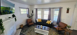 A living room with a sofa, two armchairs, a coffee table, and a fireplace. There are windows with curtains, a television, and a plant on the wall. - Recent  Remodeled UP Unit 3bedroom in West CLE (Cleveland)