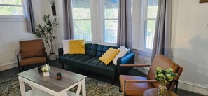Ein Wohnzimmer mit einem dunkelgrünen Sofa, zwei braunen Sesseln, einem weißen Couchtisch und einer Topfpflanze.