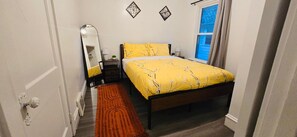 Ein Schlafzimmer mit Bett, Nachttisch, Spiegel und einem Fenster mit Vorhängen.