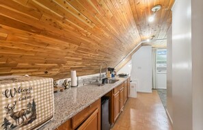 Ein Interieur einer Holzhütte mit Holzbalkendecke, einer Küchenzeile mit Spüle und einer Fußmatte.