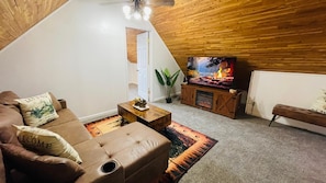 Een gezellige woonkamer met een bruine leren bank, een salontafel, een open haard en een televisie.