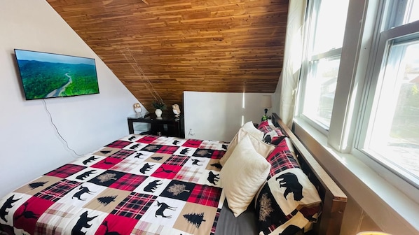Een slaapkamer met een bed, een houten plafond, een raam en een schilderij aan de muur.