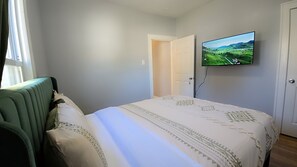 Ein Schlafzimmer mit einem Bett, einem grünen Sessel, einem an der Wand befestigten Fernseher und einer Tür zu einem anderen Raum.