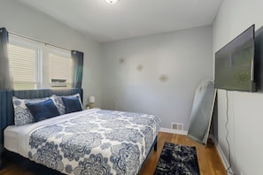 Un dormitorio con cama, televisión, ventana con persianas y un adorno en la pared.