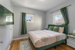 Een slaapkamer met een bed, een nachtkastje, een kledingkast, een raam met gordijnen en een deur.