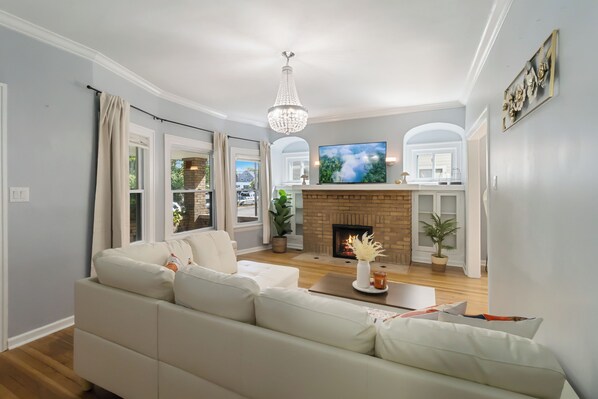 A modern living room with a fireplace, a large flat-screen TV, and a chandelier.
