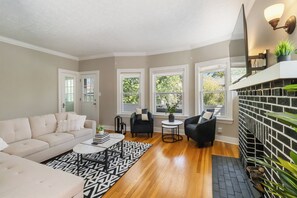 A living room with a beige sofa, black armchairs, a coffee table, and a patterned rug. - Walkable Lakewood & Rocky River up Level (Lakewood)