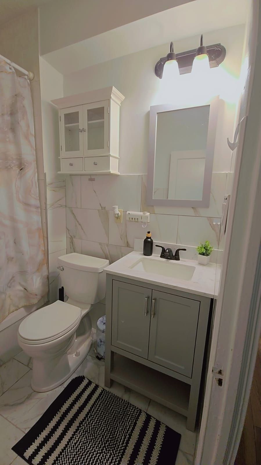 Une salle de bain comprenant des toilettes, un lavabo, un meuble de rangement, un miroir et un rideau de douche.