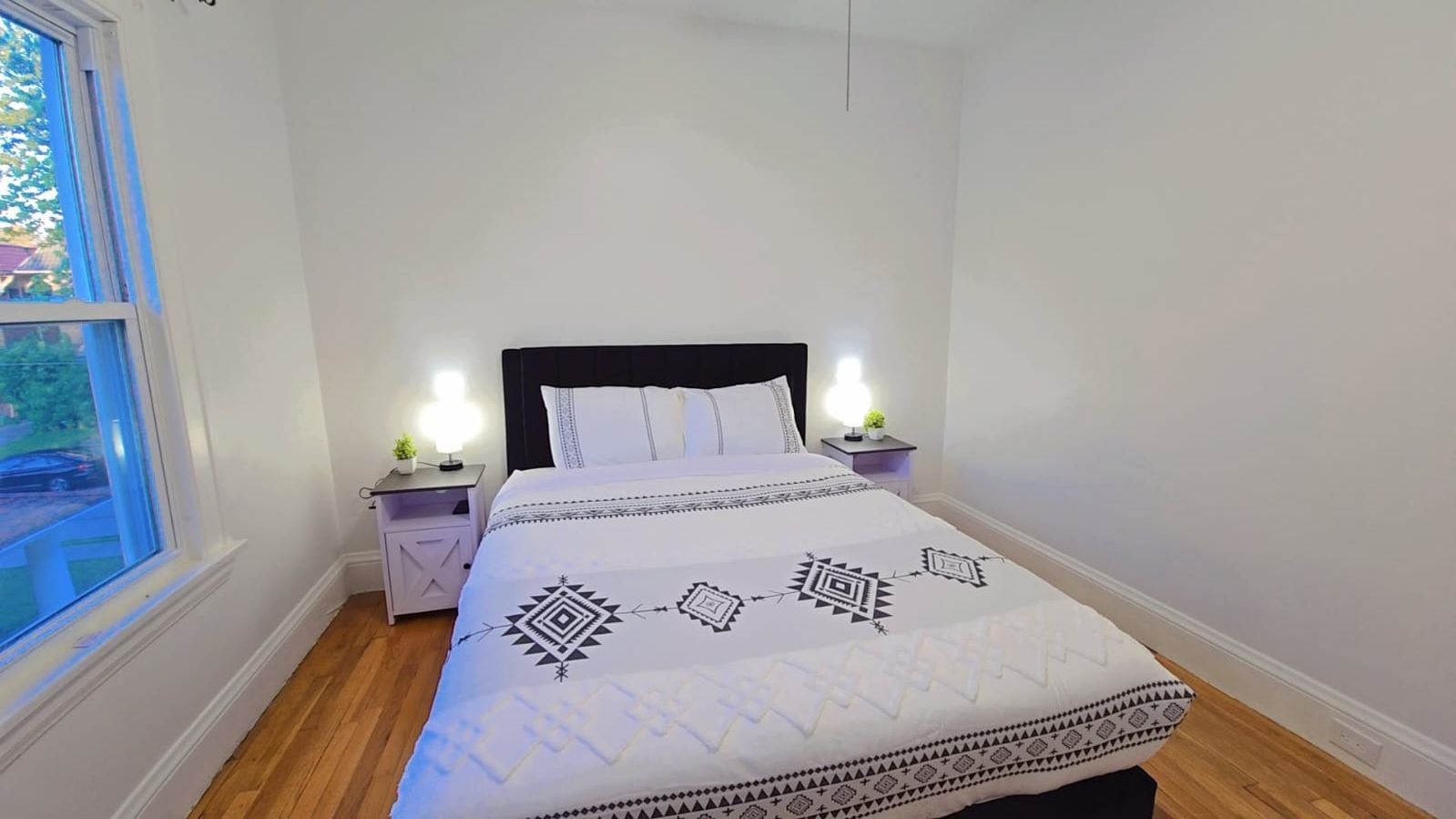 Ein Schlafzimmer mit einem Bett, zwei Nachttischen, einem Fenster und einem Beistelltisch mit einer Lampe.