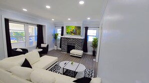 A modern living room with a white sofa, a black and white patterned rug, a fireplace, and a large window with curtains. - West BLVD Single Family house Close to Freeway for easy access to everywhere in Cleveland! (Cleveland)