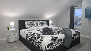 Un dormitorio moderno con una cama grande, dos mesitas de noche, una mesita auxiliar, un ventanal con vistas y un televisor de pared.