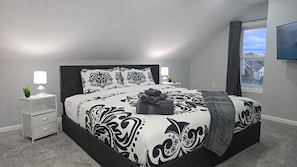 A modern bedroom with a large bed, two bedside tables, a nightstand, a window with a view, and a wall-mounted TV. - West BLVD Single Family house Close to Freeway for easy access to everywhere in Cleveland! (Cleveland)