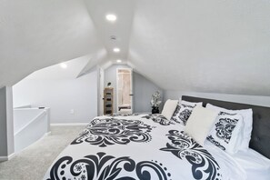 A bedroom with a sloped ceiling, a bed with patterned bedding, a nightstand, and a door leading to a bathroom. - West BLVD Single Family house Close to Freeway for easy access to everywhere in Cleveland! (Cleveland)