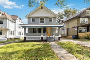 A two-story residential building with a front porch, a visible garage door, and a pathway leading to the entrance. - West BLVD Single Family house Close to Freeway for easy access to everywhere in Cleveland! (Cleveland)