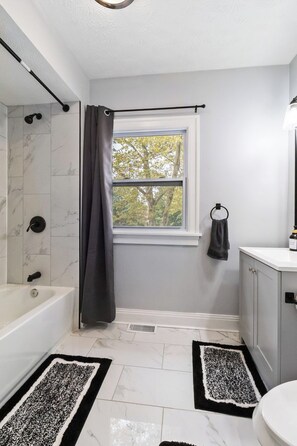 A bathroom with a bathtub, a window with a view, a towel rack, and a toilet. - West BLVD Single Family house Close to Freeway for easy access to everywhere in Cleveland! (Cleveland)