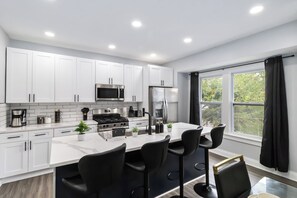 A modern kitchen with white cabinets, a stainless steel stove, and a bar area with black bar stools. - West BLVD Single Family house Close to Freeway for easy access to everywhere in Cleveland! (Cleveland)