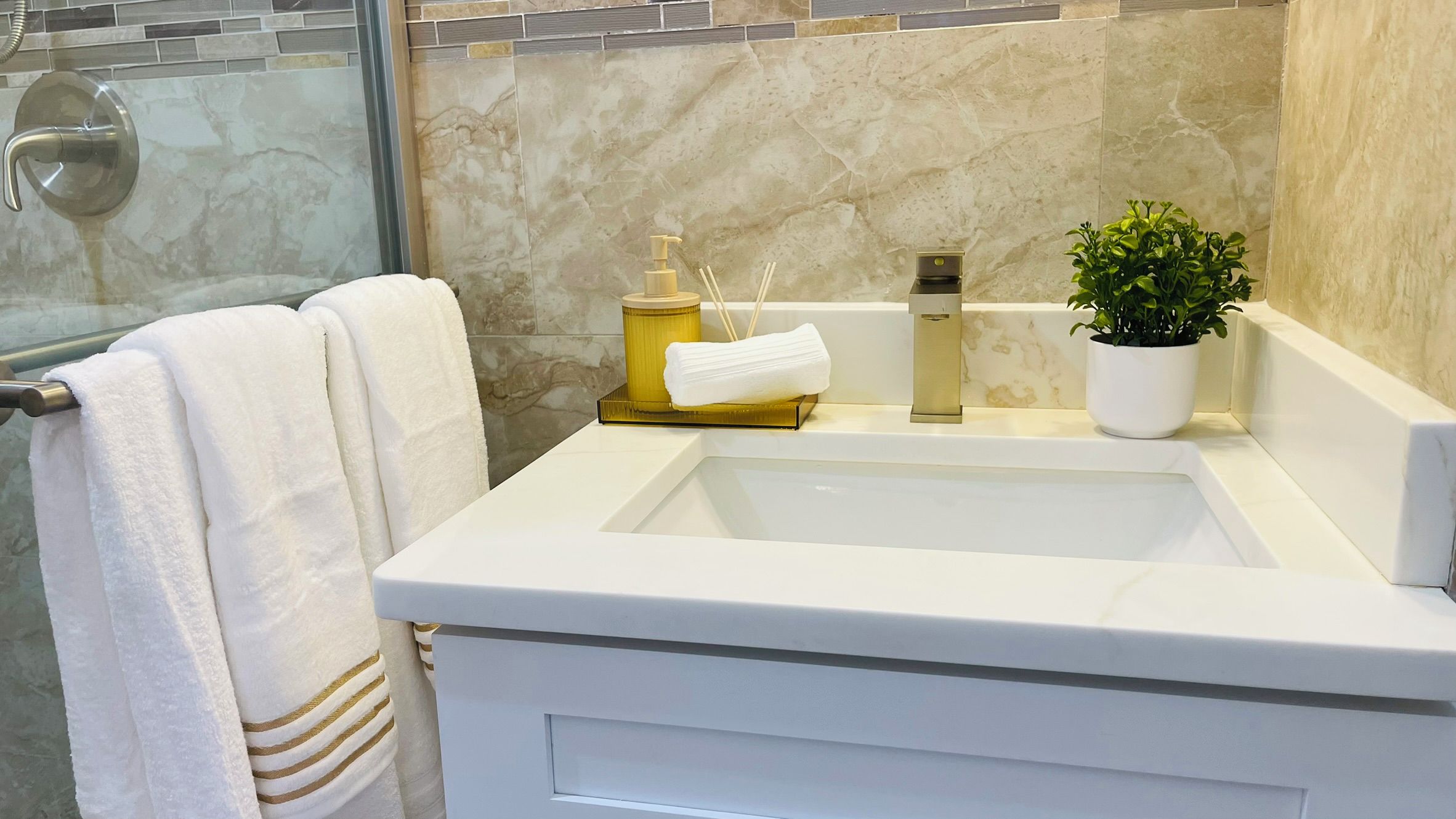 A bathroom with a white sink, a gold faucet, a potted plant, and a towel rack with a white towel.
