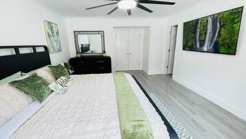 A bedroom with a bed, a dresser, a ceiling fan, a door, and a painting on the wall.