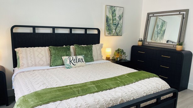 Ein Bett mit schwarzem Kopfteil, weißer Bettwäsche und grünen Akzenten, inklusive eines Kissens mit dem Schriftzug 'Relax'.