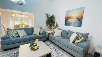 A living room with two grey sofas, a coffee table, and a painting of a sunset.