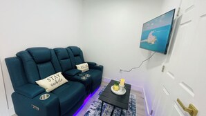 Ein Wohnzimmer mit einem türkisfarbenen Sofagarnitur, einem kleinen Tisch mit einer Kerze und einem an der Wand befestigten Fernseher.